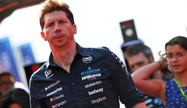 Man in a navy Williams F1 team shirt at an outdoor event, crowd in background.