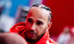 Close-up of a man with cornrow braids wearing a red hoodie, looking to the side.