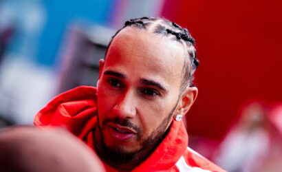 Close-up of a man with cornrow braids wearing a red hoodie, looking to the side.