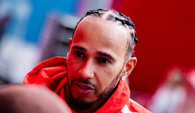 Close-up of a man with cornrow braids wearing a red hoodie, looking to the side.