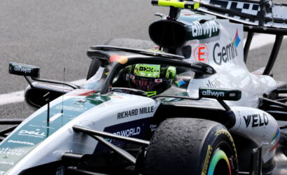 Silver Formula 1 car on a track with a neon-green helmeted driver in the cockpit and sponsor logos like Richard Mille and Dell visible on the bodywork, close-up perspective.