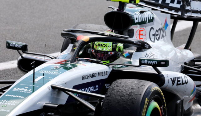Silver Formula 1 car on a track with a neon-green helmeted driver in the cockpit and sponsor logos like Richard Mille and Dell visible on the bodywork, close-up perspective.
