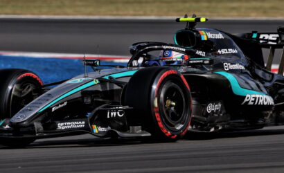 Mercedes-AMG F1 race car on track, front-left wheel in red, sponsor logos visible (Petronas, Microsoft) and teal accents on black livery.