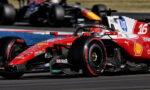 Red Ferrari Formula 1 car speeding on a race track with sponsor logos visible, in the foreground while another car blurs behind it.