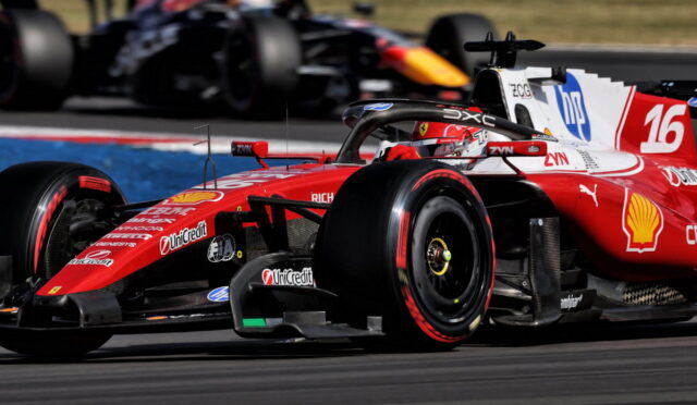 Red Ferrari Formula 1 car speeding on a race track with sponsor logos visible, in the foreground while another car blurs behind it.