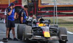 Red Bull Formula 1 car in the pit lane with crew members examining the tires behind a safety fence.
