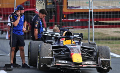 Red Bull Formula 1 car in the pit lane with crew members examining the tires behind a safety fence.