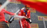 Ferrari driver on a podium spraying champagne, teammate holding a Moët bottle; sponsor banners in the background.