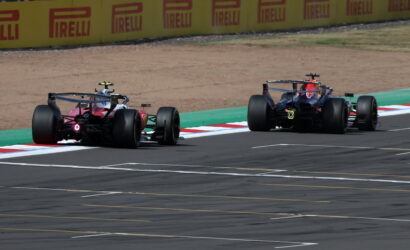 Two Formula 1 cars race side by side on a track, with yellow Pirelli barriers in the background.
