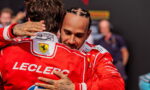 Two Formula 1 drivers in red Ferrari racing suits hug each other, their faces close in a moment of celebration, with one jacket showing a crest and the word 'LECLERC' on the back.
