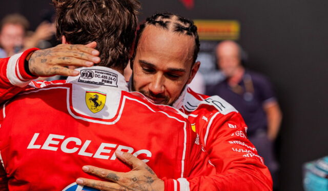 Two Formula 1 drivers in red Ferrari racing suits hug each other, their faces close in a moment of celebration, with one jacket showing a crest and the word 'LECLERC' on the back.