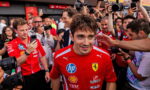 Ferrari driver in a red team shirt surrounded by reporters and photographers taking pictures.