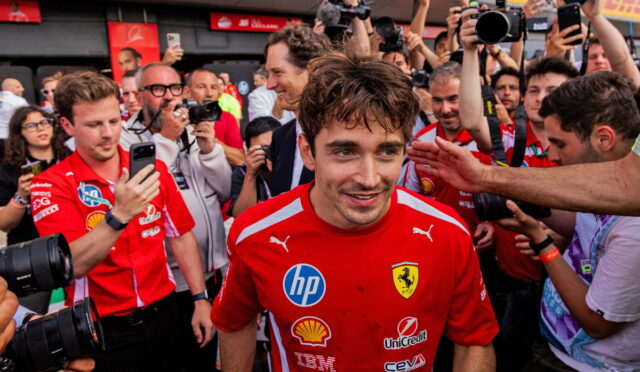 Ferrari driver in a red team shirt surrounded by reporters and photographers taking pictures.