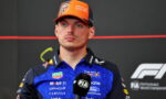 Portrait of a Formula 1 driver in a blue sponsor-laden uniform and orange cap, speaking into a microphone.