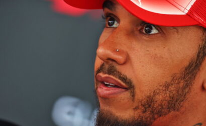 Close-up of a man with a nose piercing wearing a red cap, looking upward to the left.