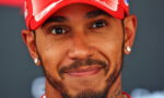 Close-up portrait of a smiling man wearing a red cap, with facial hair and diamond earrings.