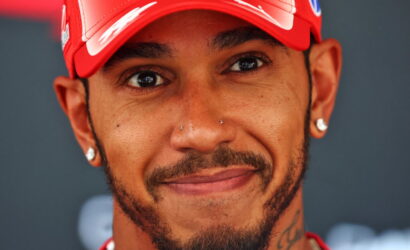 Close-up portrait of a smiling man wearing a red cap, with facial hair and diamond earrings.