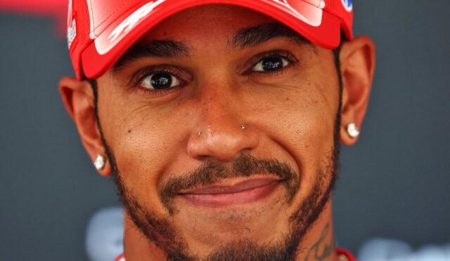 Close-up portrait of a smiling man wearing a red cap, with facial hair and diamond earrings.