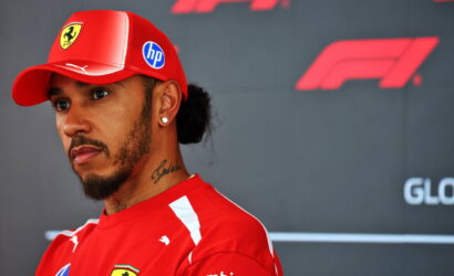 Portrait of a man in a red Ferrari cap and matching shirt at a Formula 1 event, looking to the left with a serious expression.