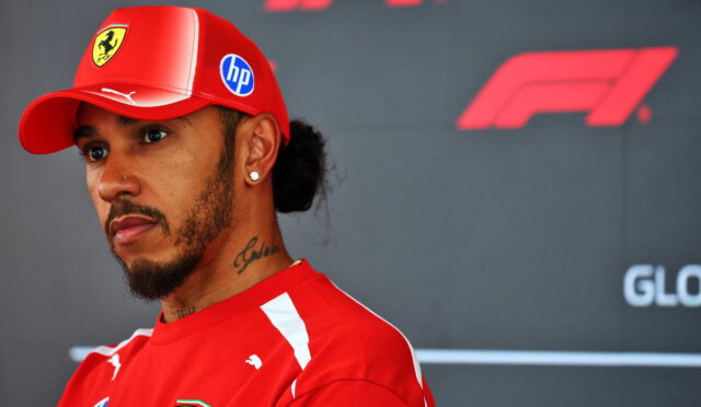 Portrait of a man in a red Ferrari cap and matching shirt at a Formula 1 event, looking to the left with a serious expression.