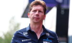 Portrait of a man in a navy blue Williams F1 polo with sponsor logos, outdoors, looking to the left.