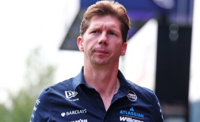 Portrait of a man in a navy blue Williams F1 polo with sponsor logos, outdoors, looking to the left.