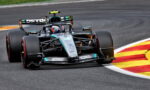 Mercedes Formula One car (Petronas livery) corners a race track, tires gripping the asphalt near red-yellow curbs