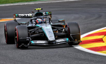 Mercedes Formula One car (Petronas livery) corners a race track, tires gripping the asphalt near red-yellow curbs