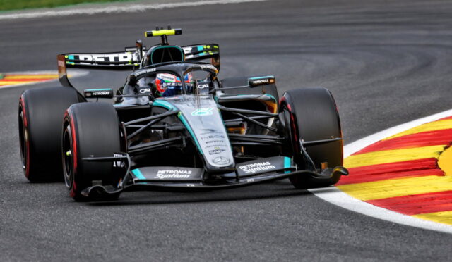 Mercedes Formula One car (Petronas livery) corners a race track, tires gripping the asphalt near red-yellow curbs