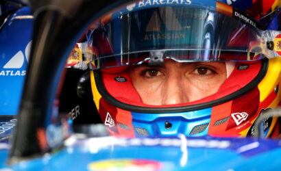Close-up view of a race car driver's focused eyes behind a blue visor and red helmet accents in the cockpit.