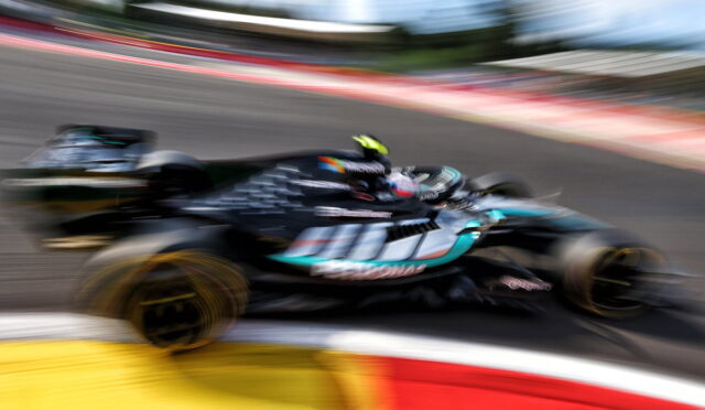 Blurred action shot of a teal and black Formula 1 car racing around a bend on a track, motion blur emphasizing speed and curvature of the circuit edge in foreground.