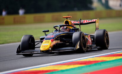 Red Bull Formula 1 car speeding on track, leaning into a corner with colorful striped curbs in the foreground.
