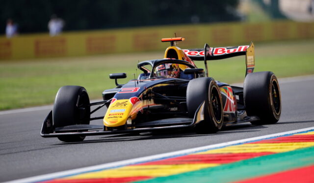 Red Bull Formula 1 car speeding on track, leaning into a corner with colorful striped curbs in the foreground.