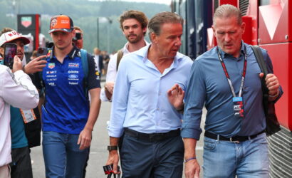 Group of men walking along a race pit lane; two in front converse while others, including a photographer, look on