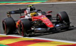 Red Formula 1 race car turning on track, colorful curbs in the foreground, sponsor logos visible on the bodywork.