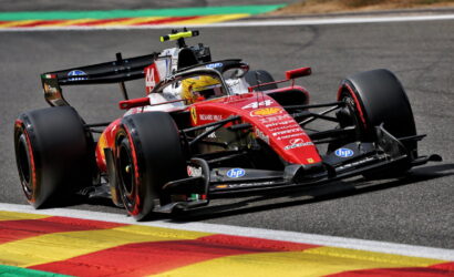 Red Formula 1 race car turning on track, colorful curbs in the foreground, sponsor logos visible on the bodywork.