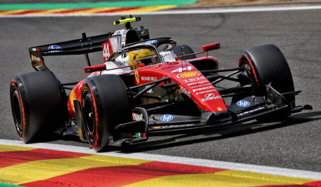Red Formula 1 race car turning on track, colorful curbs in the foreground, sponsor logos visible on the bodywork.