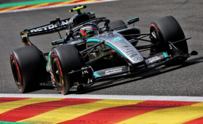 Mercedes Formula 1 car with Petronas livery turns through a corner on a race track, colorful curbs in the foreground