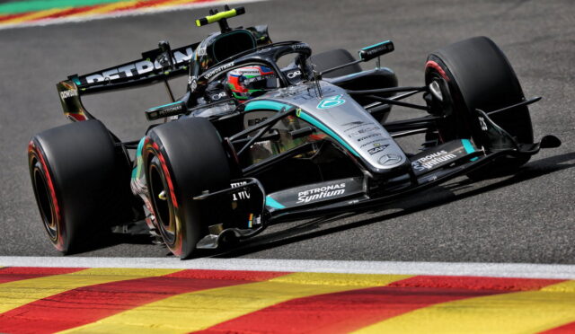 Mercedes Formula 1 car with Petronas livery turns through a corner on a race track, colorful curbs in the foreground