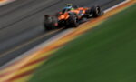 Orange Formula 1 car speeding along a race track with heavy motion blur, cornering on the tarmac.