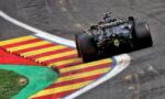 Formula race car navigating a sharp turn on a track with red, yellow, and blue curbs; 'CROWD STRIKE' branding on the rear wing.
