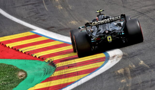 Formula race car navigating a sharp turn on a track with red, yellow, and blue curbs; 'CROWD STRIKE' branding on the rear wing.