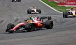 Red Ferrari Formula 1 car leading a race on the track with other cars behind it and red barriers in the background