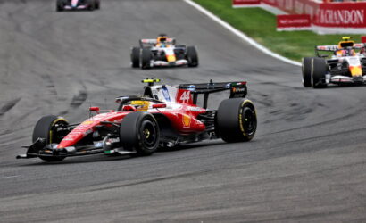 Red Ferrari Formula 1 car leading a race on the track with other cars behind it and red barriers in the background