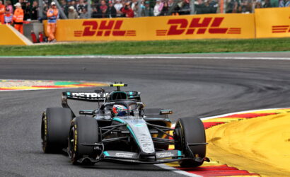 Race car speeding around a corner on a track with bright yellow DHL barriers in the background and a cheering crowd watching from the stands
