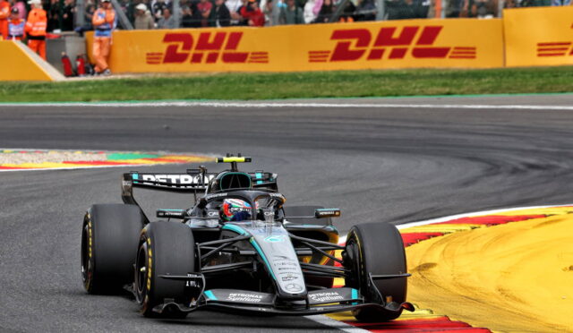 Race car speeding around a corner on a track with bright yellow DHL barriers in the background and a cheering crowd watching from the stands