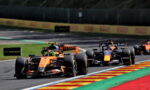Orange Formula 1 car leading a race with trailing cars on a curvy track and colorful painted runoff areas.