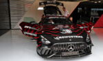 Black Mercedes AMG Safety Car with red and gray graphic livery, doors open, in a showroom with crew members nearby; CROWDSTRIKE branding visible on hood and sides.