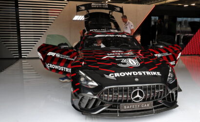 Black Mercedes AMG Safety Car with red and gray graphic livery, doors open, in a showroom with crew members nearby; CROWDSTRIKE branding visible on hood and sides.