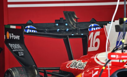 Rear wing of a red Formula 1 car with the number 16 and sponsor logos, in a garage or workshop setting.